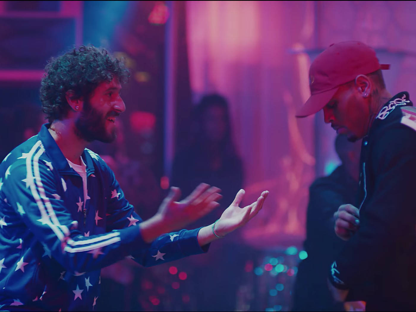 《怪誕星期五》Lil Dicky與Chris Brown音樂錄影帶 壁紙 — 兩個男人在霓虹燈俱樂部中交談，紫色和藍色的燈光在潮濕的表面上反射。