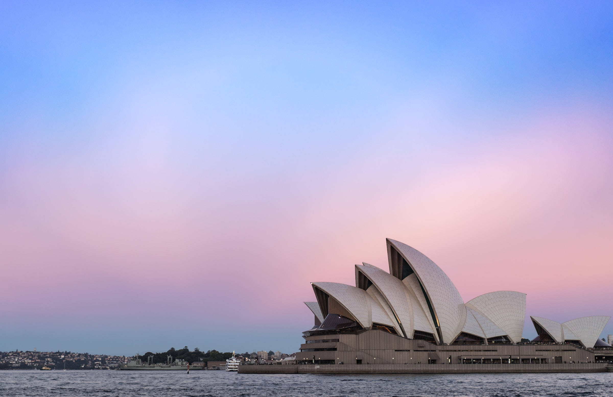 Sydney 桌布 壁紙 — 悉尼歌劇院的帆船造型，映襯著柔和粉紅與藍色的暮色天空，下方是平靜的港灣水面。