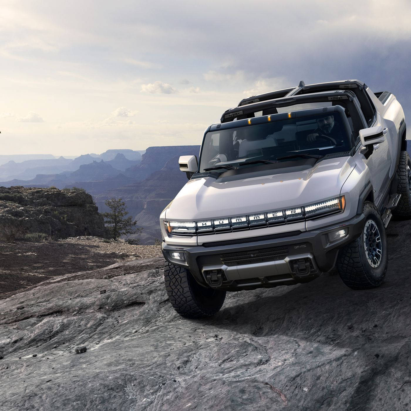 銀色Hummer EV SUV停放在岩石峽谷地形上，背景有層疊的平頂山。