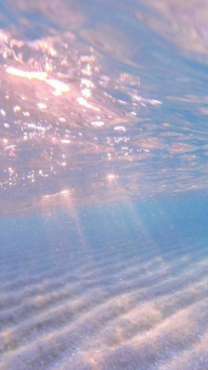 悠閒海灘一日遊 壁紙 — 陽光穿過清澈的藍色海水，在沙質海底投射出閃爍的光線。
