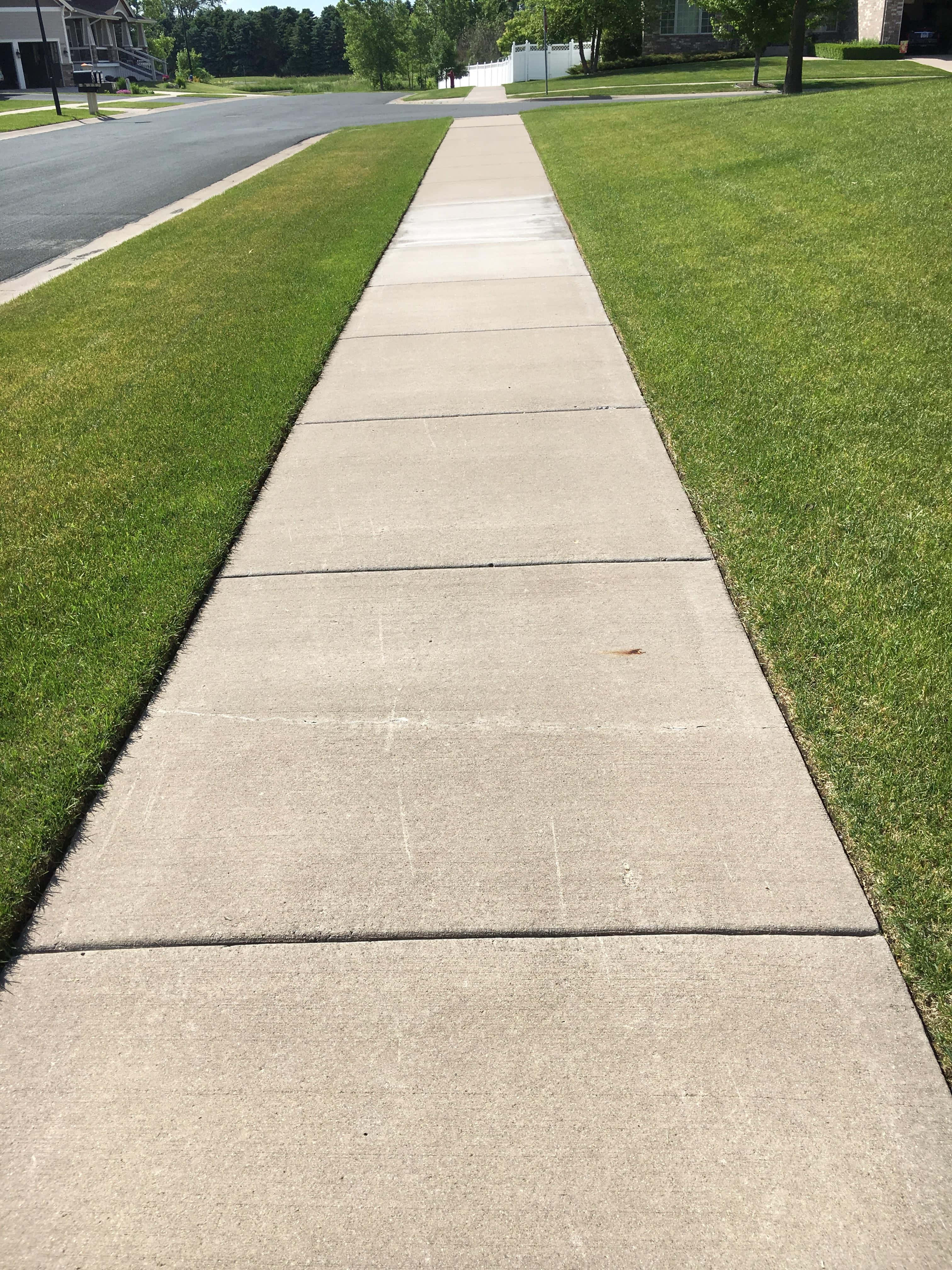 悠閒漫步於人行道上 壁紙 — 一條筆直的混凝土行人路穿過陽光明媚的郊區社區，兩旁是綠色的草坪和樹木。