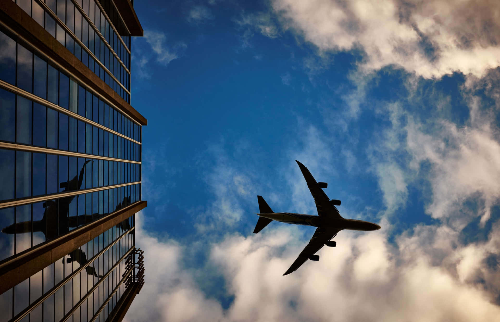 飛機飛過現代玻璃建築，天空中有雲。