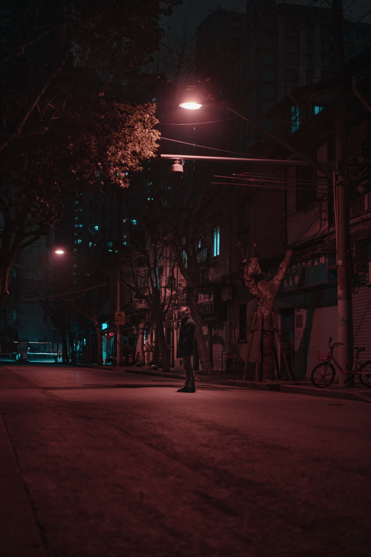 一個孤獨的人夜晚站在昏暗的城市街道上，在一盞紅色街燈下。