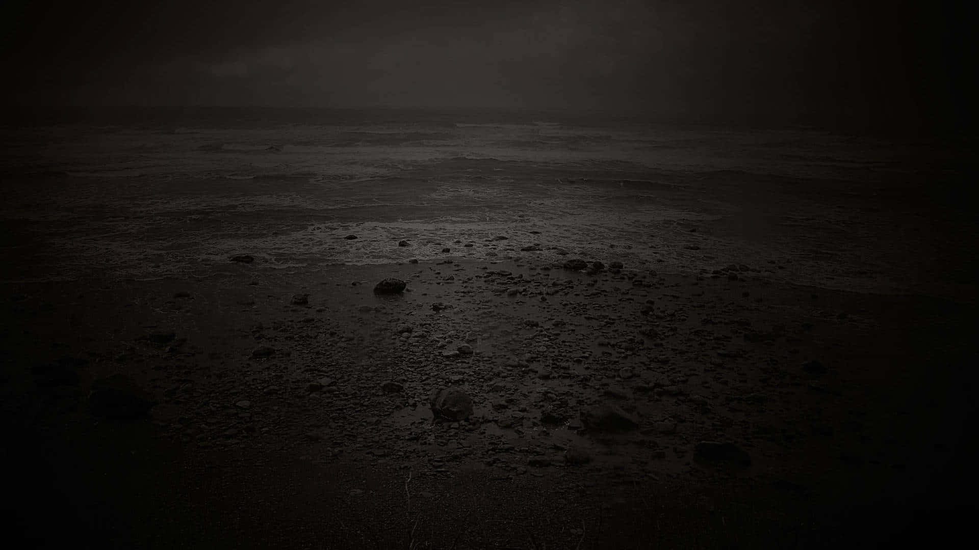 夜晚陰暗的海灘，波浪拍打，岩石散落，暴風雨天空。