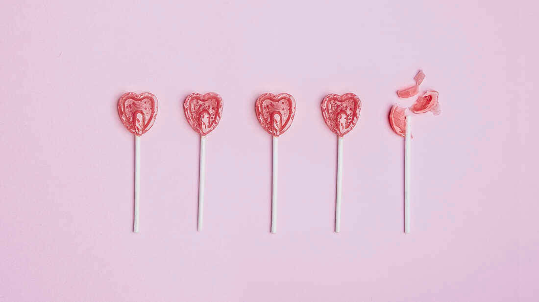 情人節棒棒糖在粉紅背景上 壁紙 — 五個心形粉紅色棒棒糖排成一排，放在柔和的粉紅色背景上，其中一個被部分吃掉。
