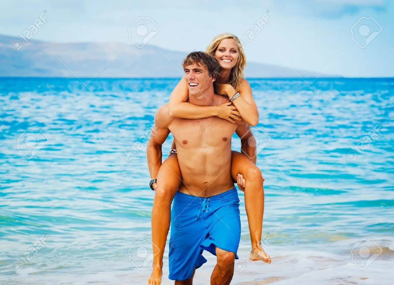 陽光明媚的海灘上，男子背著女子的快樂情侶。