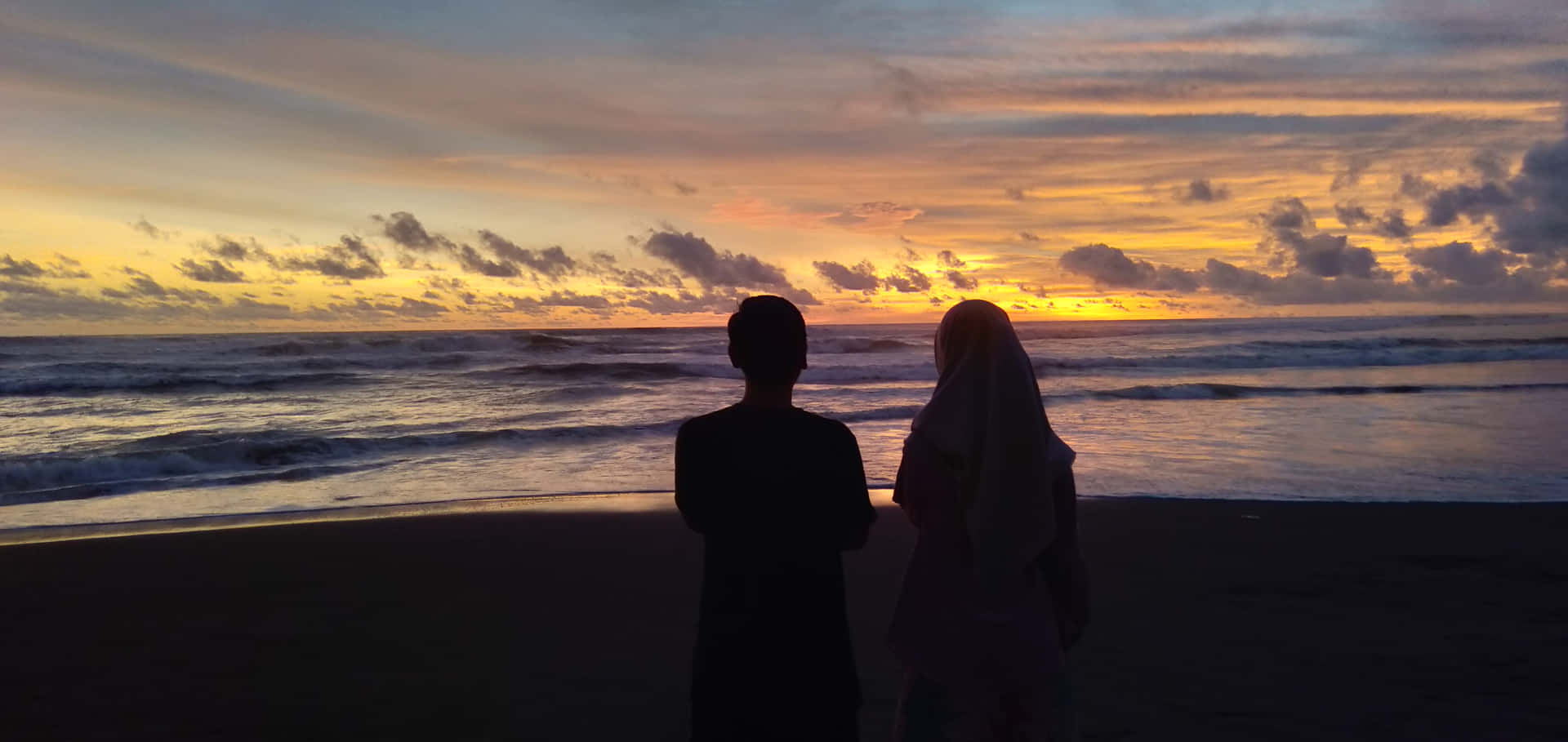 沙灘上情侶剪影觀賞海上多彩夕陽