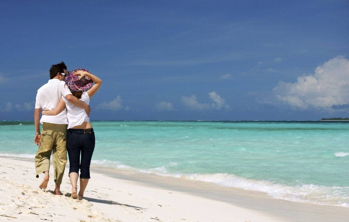 一對情侶在陽光明媚的熱帶海灘上漫步，海水碧綠，沙灘潔白。