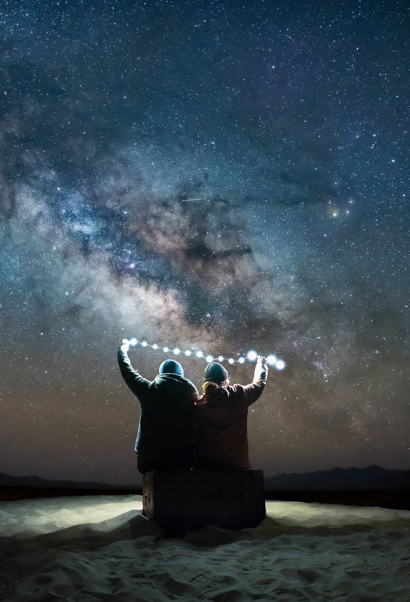 兩個人在沙漠中星空下舉著燈光。