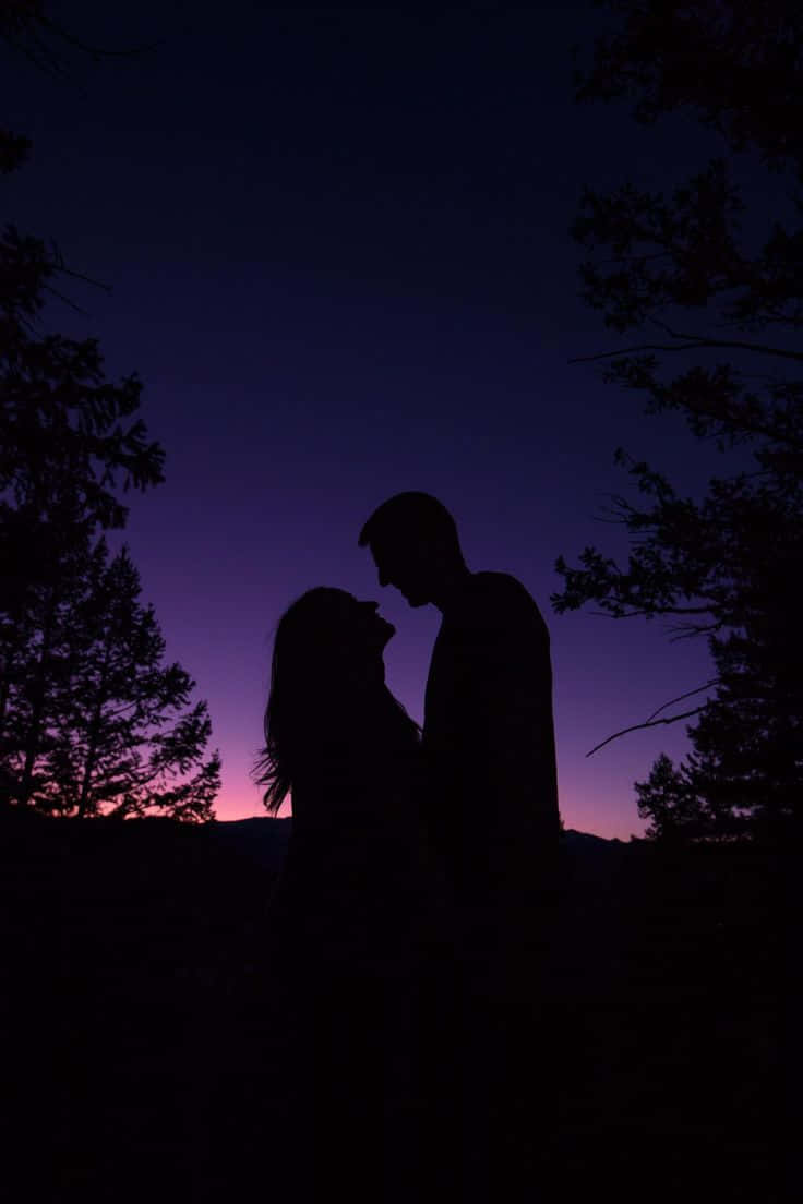 黃昏時分，情侶剪影即將親吻，背景為紫色天空和樹木