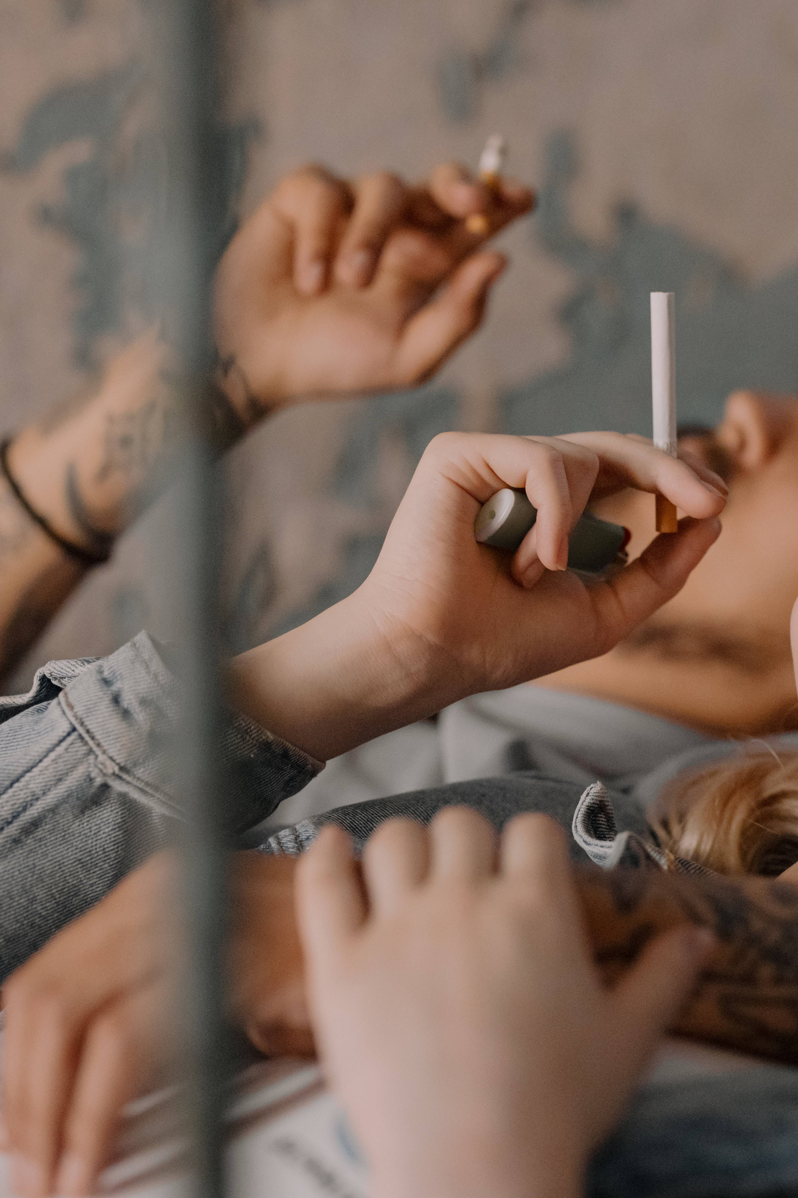情侶躺平交換香煙 壁紙 — 一個有紋身的人躺著吸煙，透過玻璃屏障觀看，色調柔和低沉。