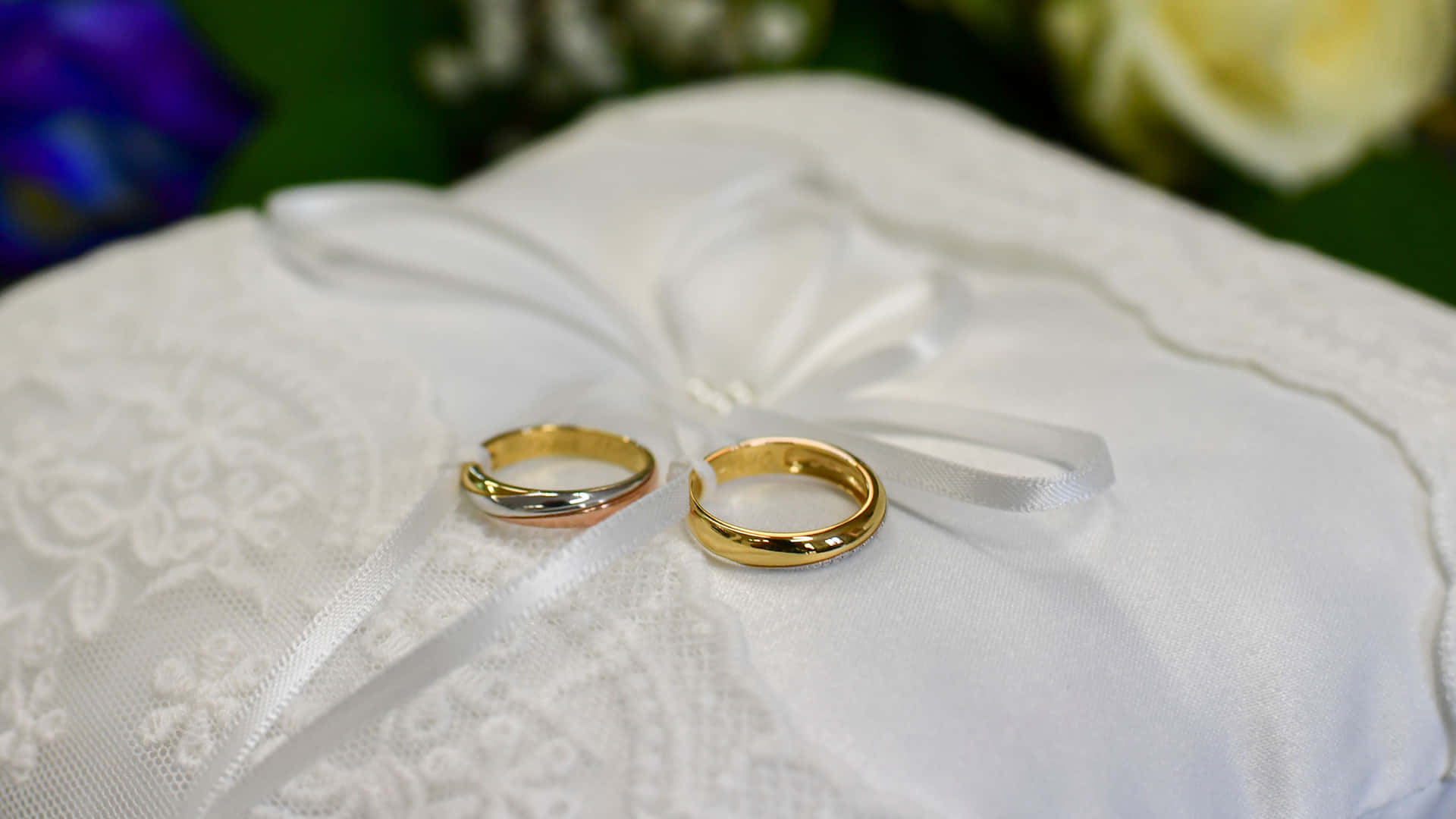 兩枚結婚戒指在白色蕾絲枕頭上，帶有花卉背景。