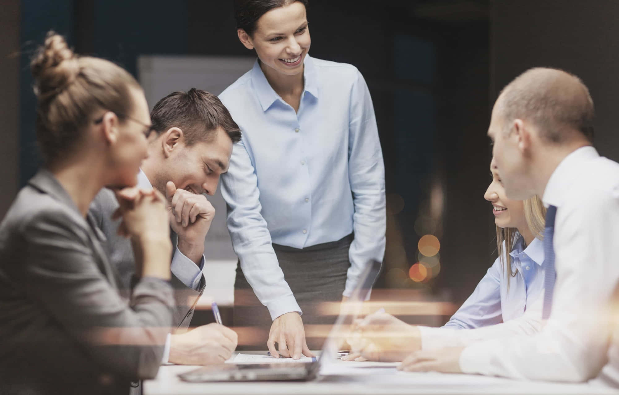 想達成職業目標？從 Coaching 課程開始吧！ 壁紙 — 四位專業人士圍繞會議桌協作，背景有溫暖的散景燈光。