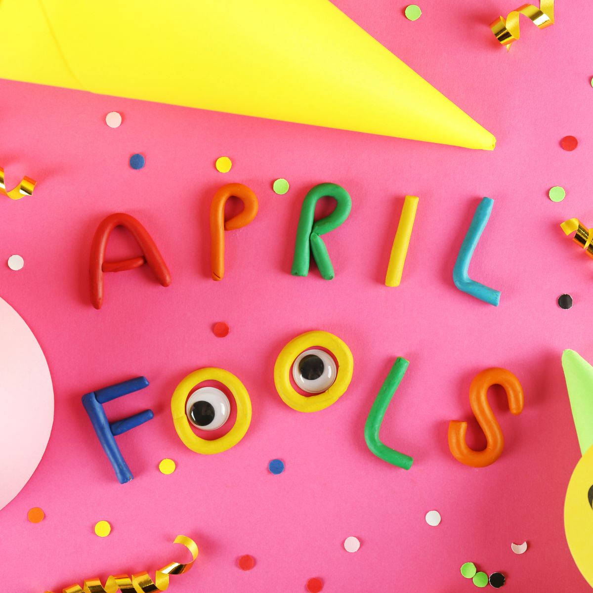 April Fools 用色彩繽紛的黏土字母拼出，帶有凸眼，背景為粉紅色。