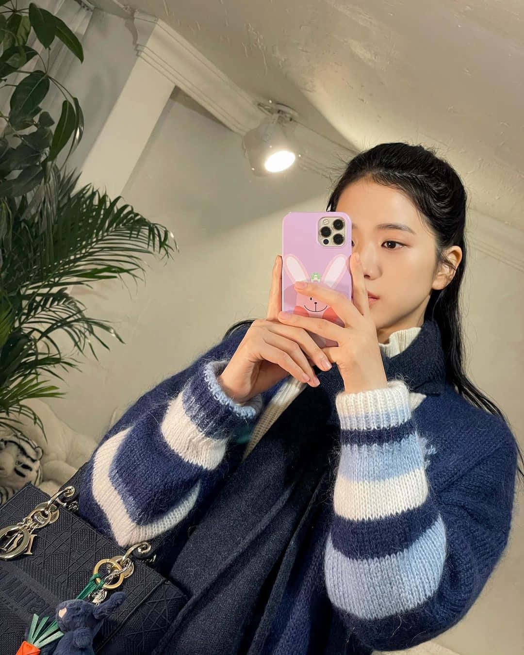 愛上自己的倒影 💕 壁紙 — 一位身穿藍白條紋針織毛衣的年輕女性，用粉紅色兔子手機殼對著鏡子自拍。