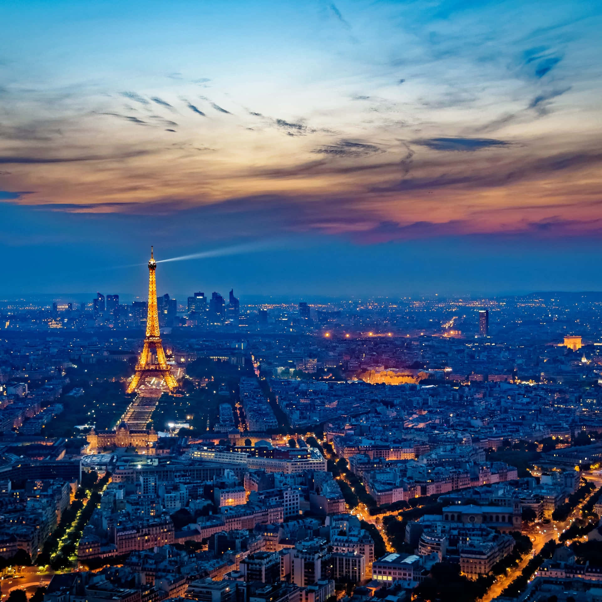 黃昏時分的巴黎城市景觀，艾菲爾鐵塔亮起燈光，天空染上橙色和紫色。