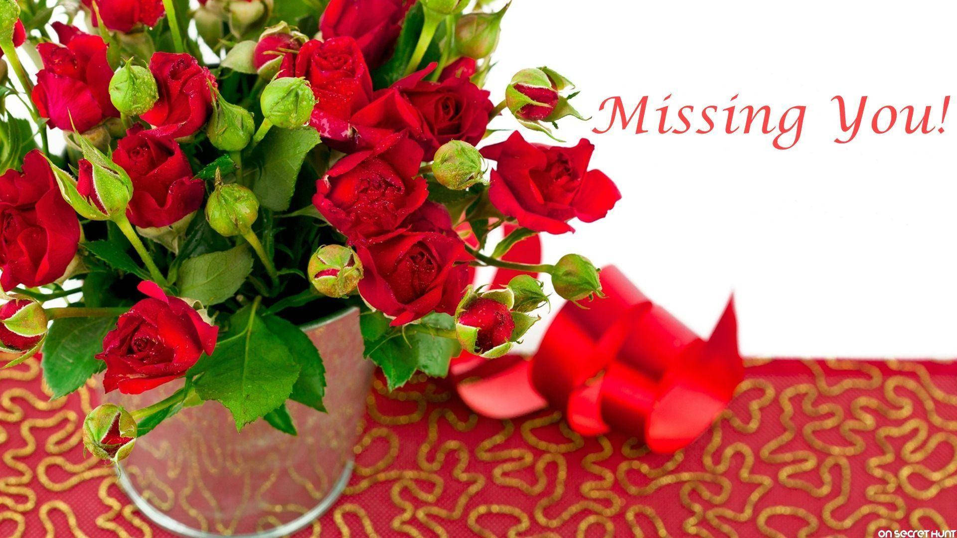 花瓶中的紅玫瑰，帶有紅色絲帶和「Missing You!」文字，放在圖案布上。