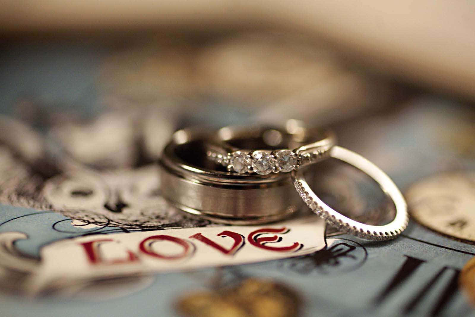 愛之鑽石銀色婚戒 壁紙 — 兩枚結婚戒指在復古地圖上閃耀，上面有紅色字體的love字樣。
