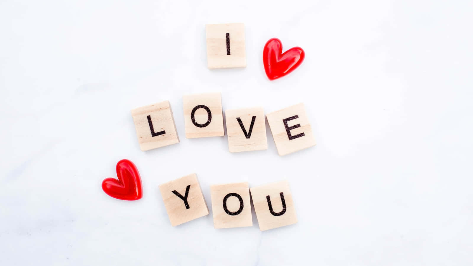愛你 壁紙 — 木製方塊在潔白的大理石表面上拼出「I LOVE YOU」，並帶有紅色心形吊飾。