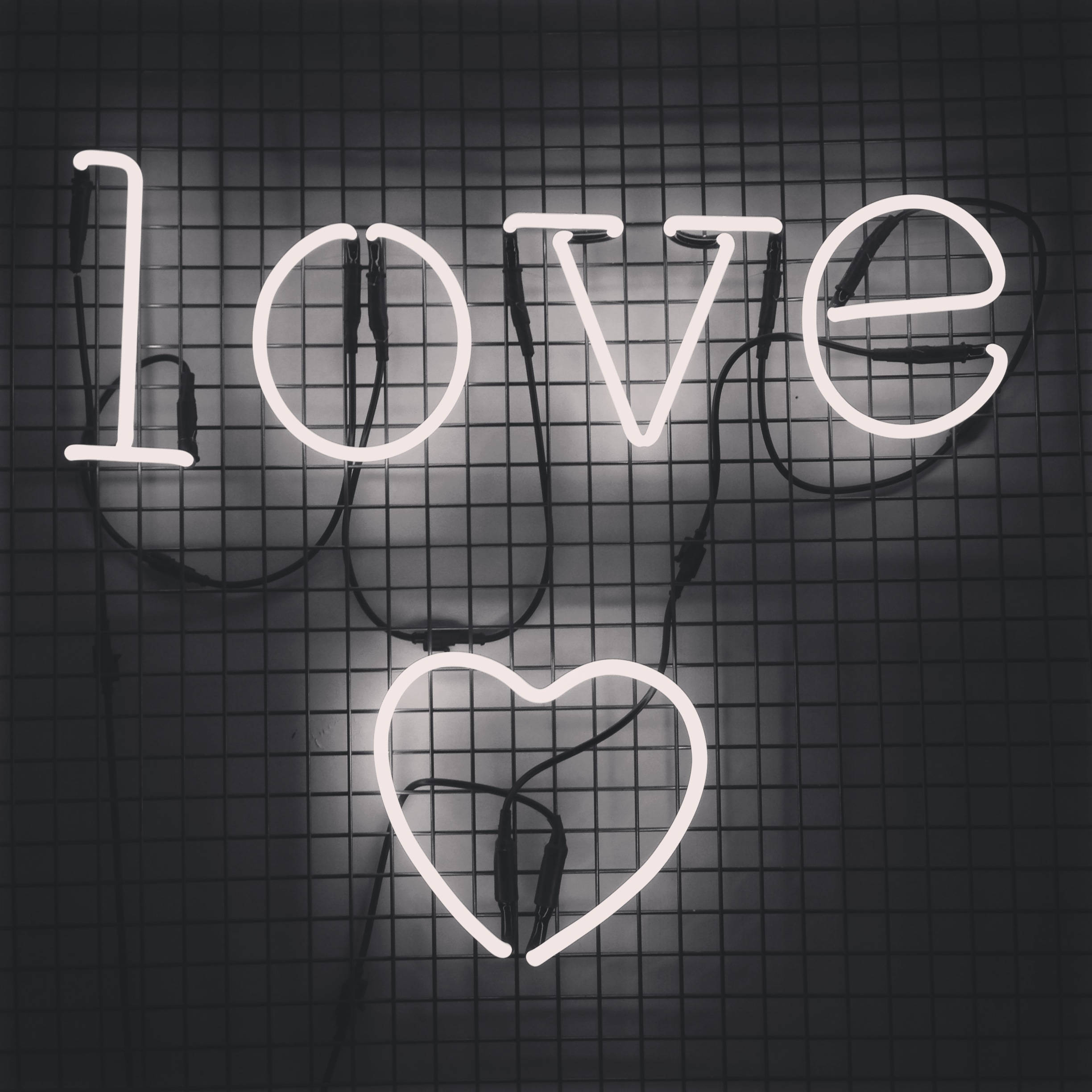 愛在格網白霓虹美學 壁紙 — 一個發光的白色霓虹燈牌，拼出 'love'，下方有一個心形，安裝在深色格柵牆上。