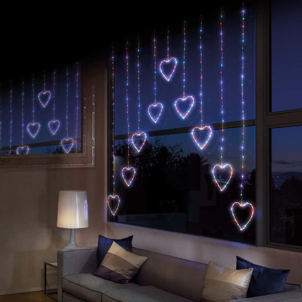 愛在給予與分享中成長 壁紙 — 舒適的客廳在夜晚裝飾著從窗戶垂下的發光心形燈串。
