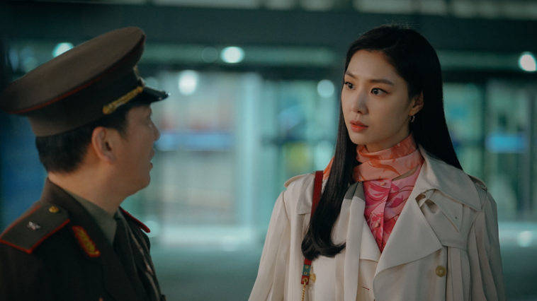 身穿風衣和圍巾的女性在室內黃昏時分面對身穿軍裝的男性。