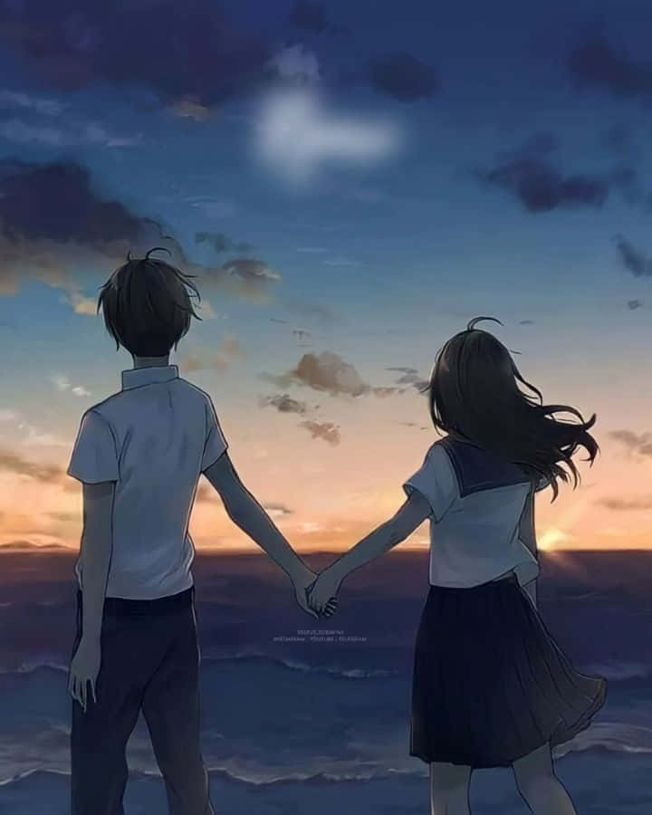 兩個青少年手牽手觀看海洋上的日落和心形雲朵