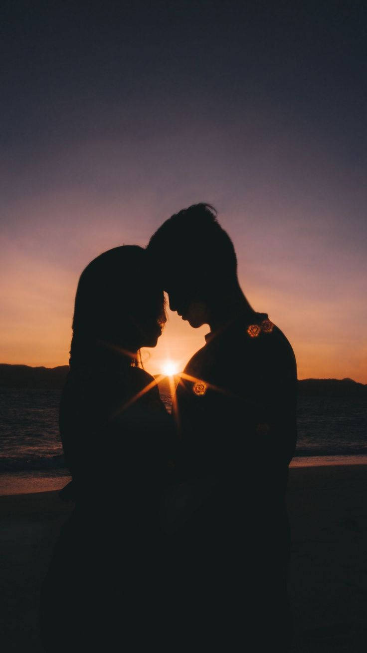 愛戀情侶剪影 壁紙 — 剪影情侶在寧靜的海灘上，夕陽在他們身後落下，分享親密時刻。