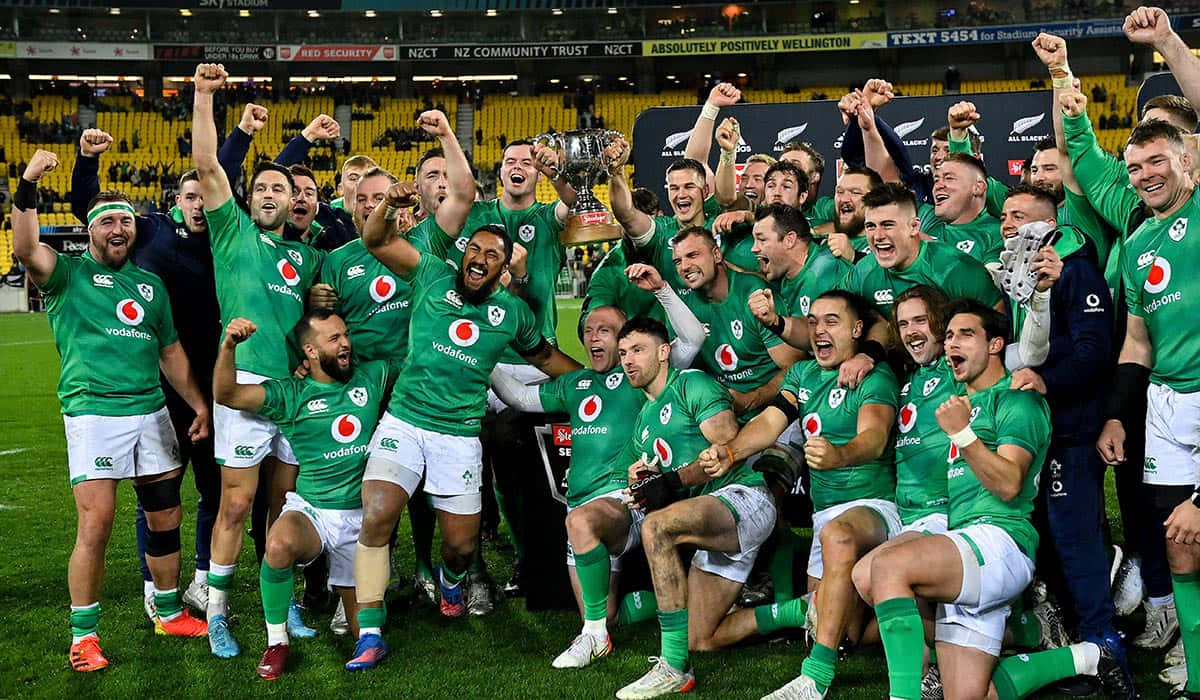 Ireland Rugby 桌布 壁紙 — 愛爾蘭欖球隊身穿綠色球衣在球場燈光下的草地上高舉獎盃慶祝勝利。