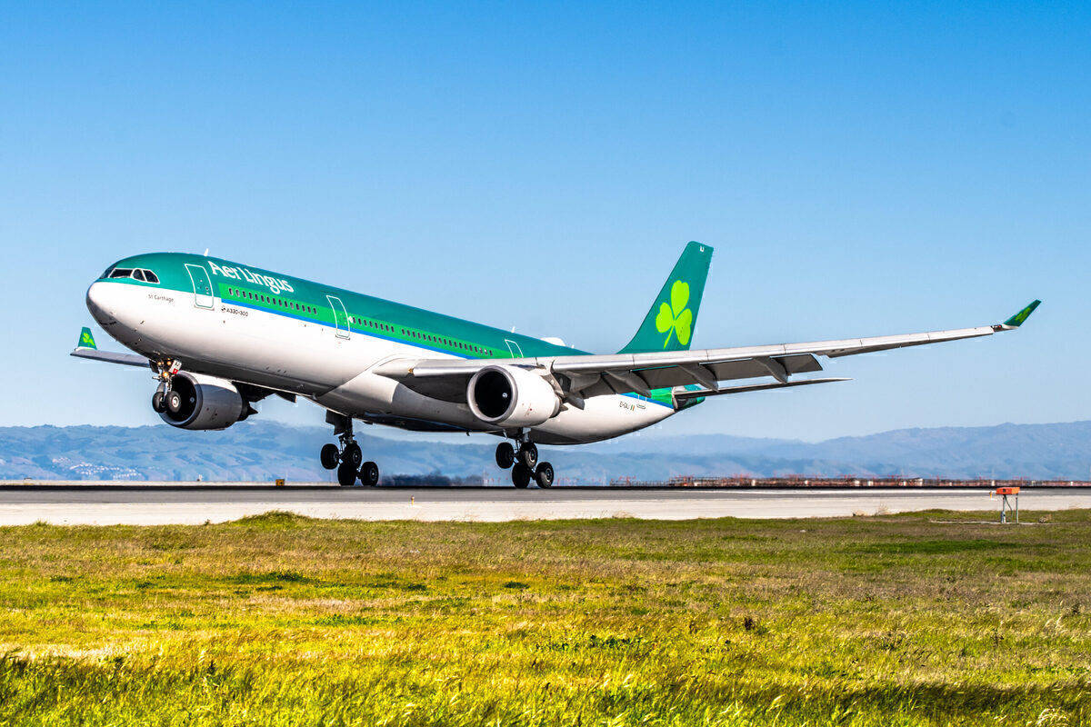 愛爾蘭航空飛機從跑道起飛，背景有綠色草地和山丘。