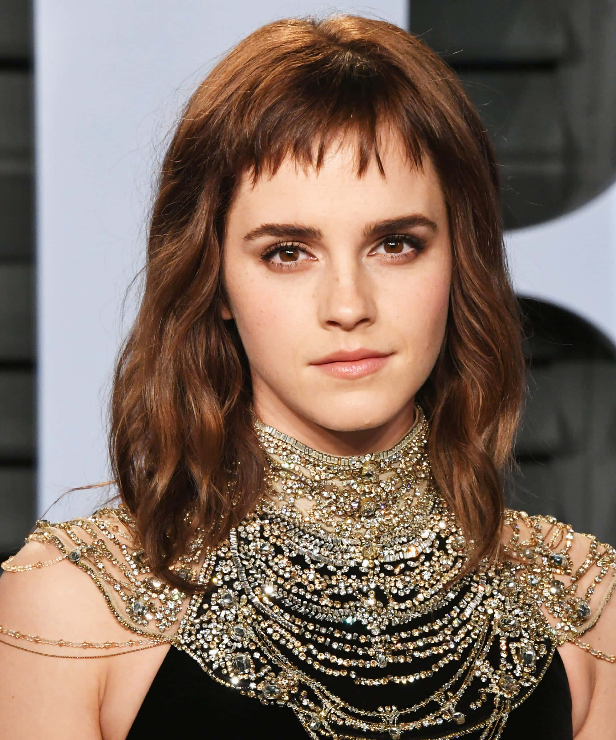 Emma Watson 桌布 壁紙 — 愛瑪屈臣以沉穩表情直視前方，身穿飾有精緻肩部細節的華麗黑金鑲寶石長裙。