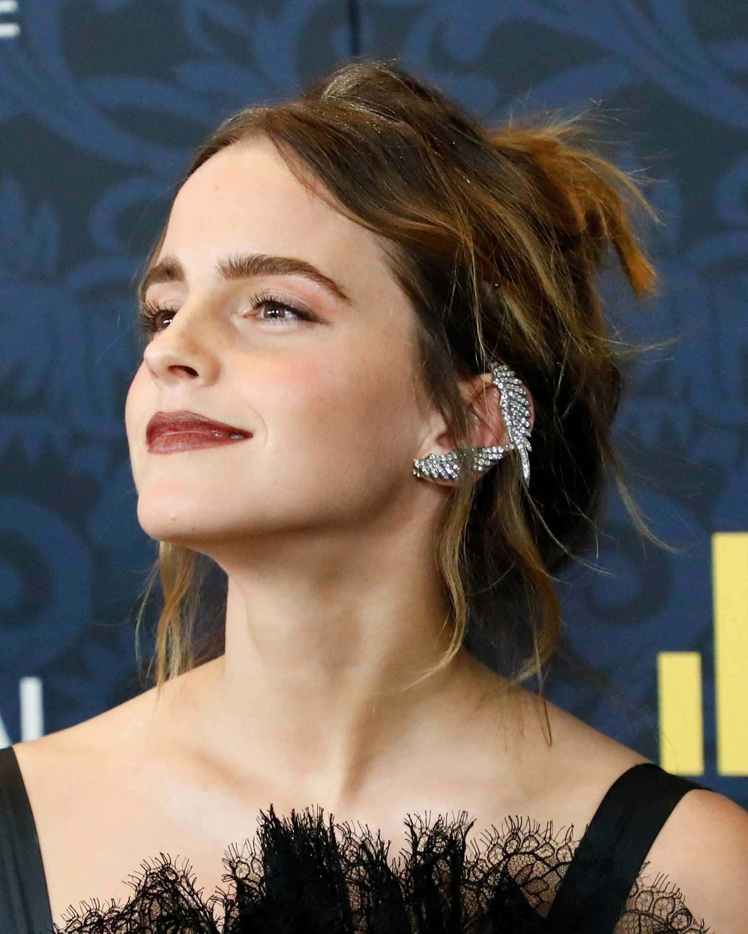 Emma Watson 桌布 壁紙 — 愛瑪屈臣抬頭微笑，戴著閃亮銀色耳環和黑色蕾絲上衣，背景為深藍色圖案。