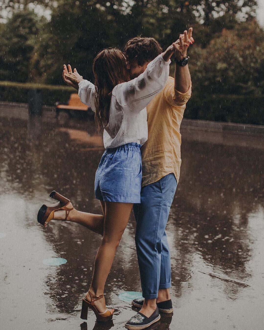 愛的庇護所 壁紙 — 一對情侶在雨中濕漉漉的路面上快樂地跳舞，背景有樹木。