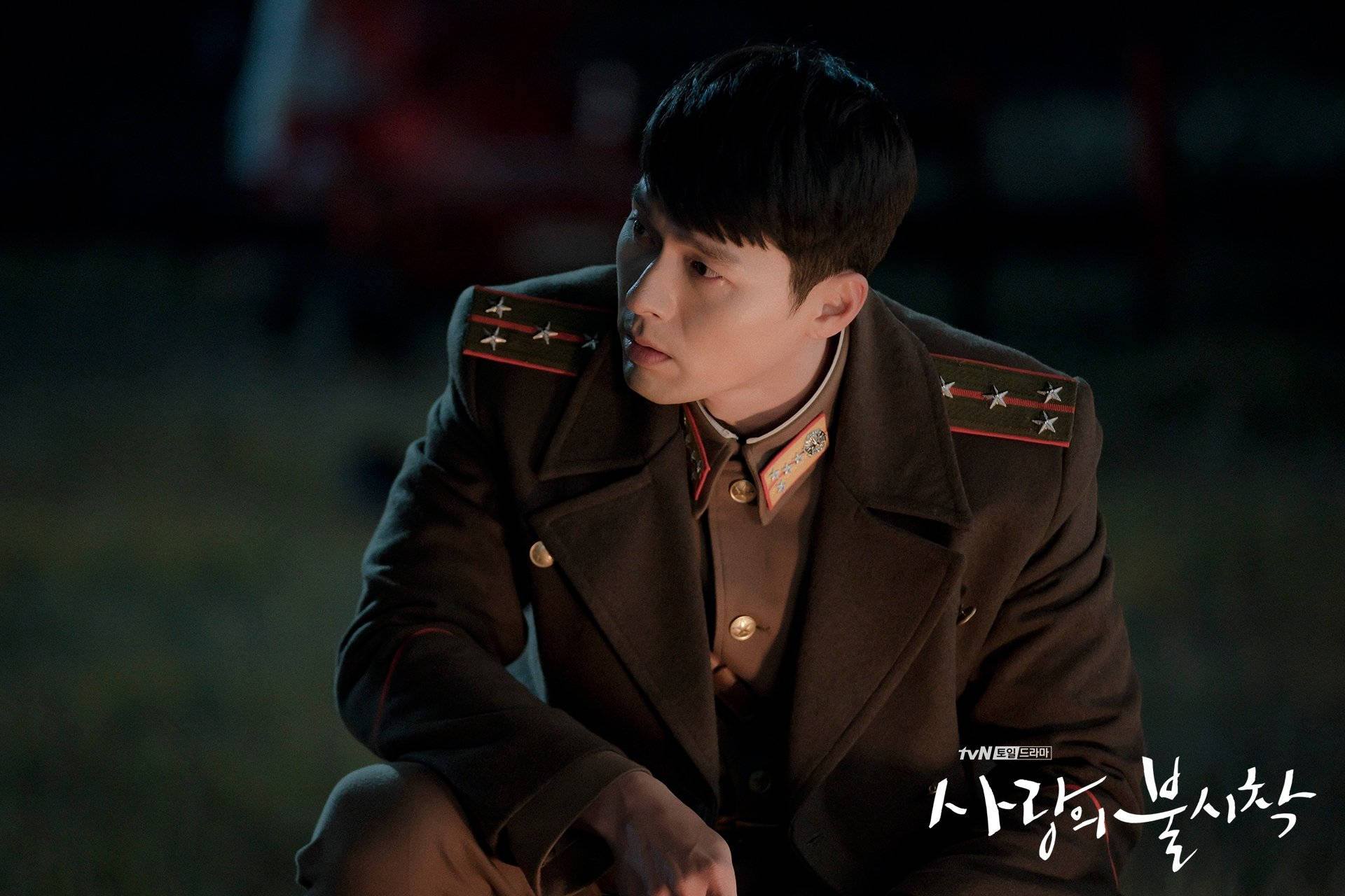 《愛的迫降》李政赫軍裝威嚴形象 壁紙 — 一名身穿深色軍服的男子在昏暗的夜燈下坐著，表情嚴肅。