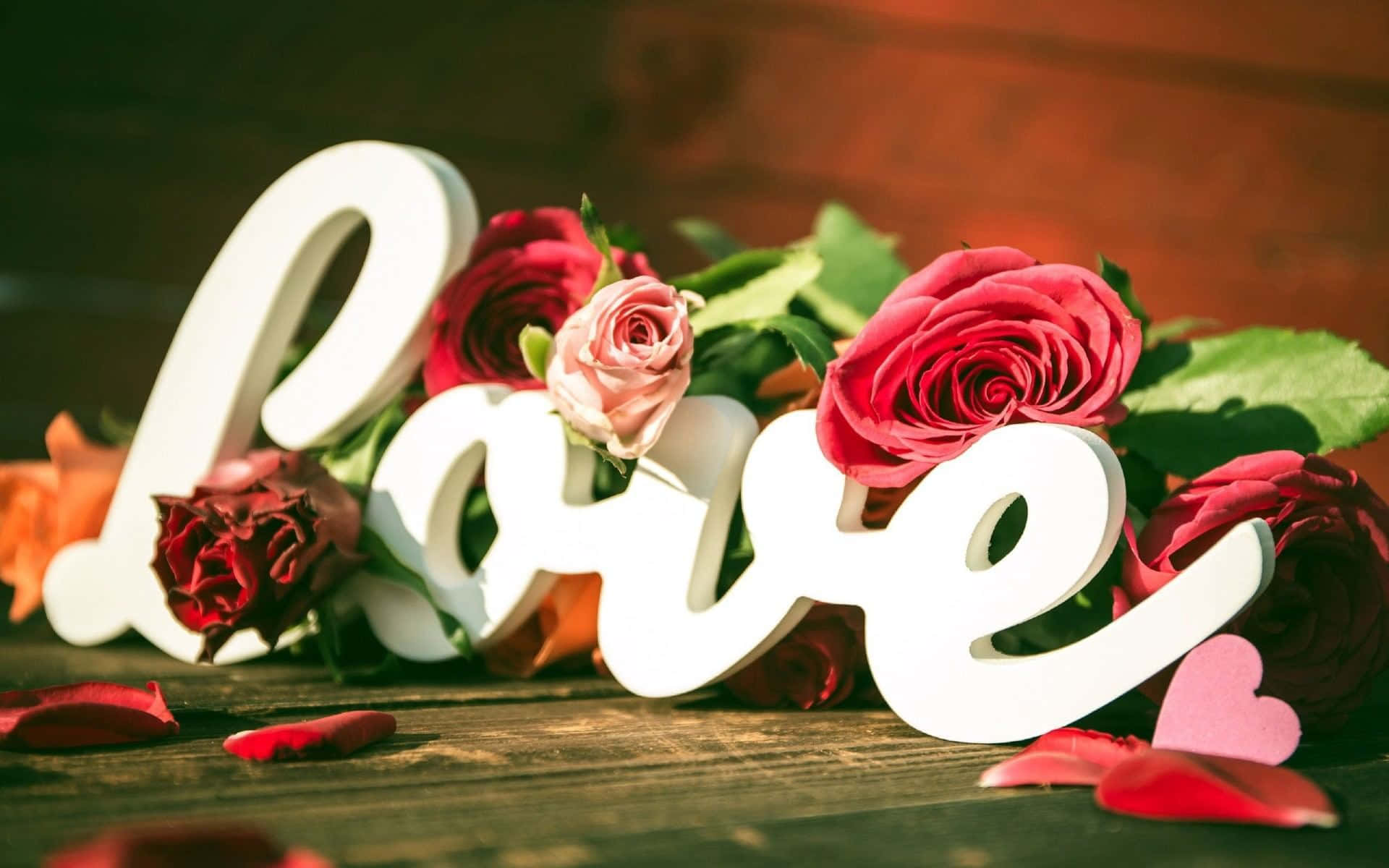 白色 'love' 字母被紅粉玫瑰環繞在木桌上。