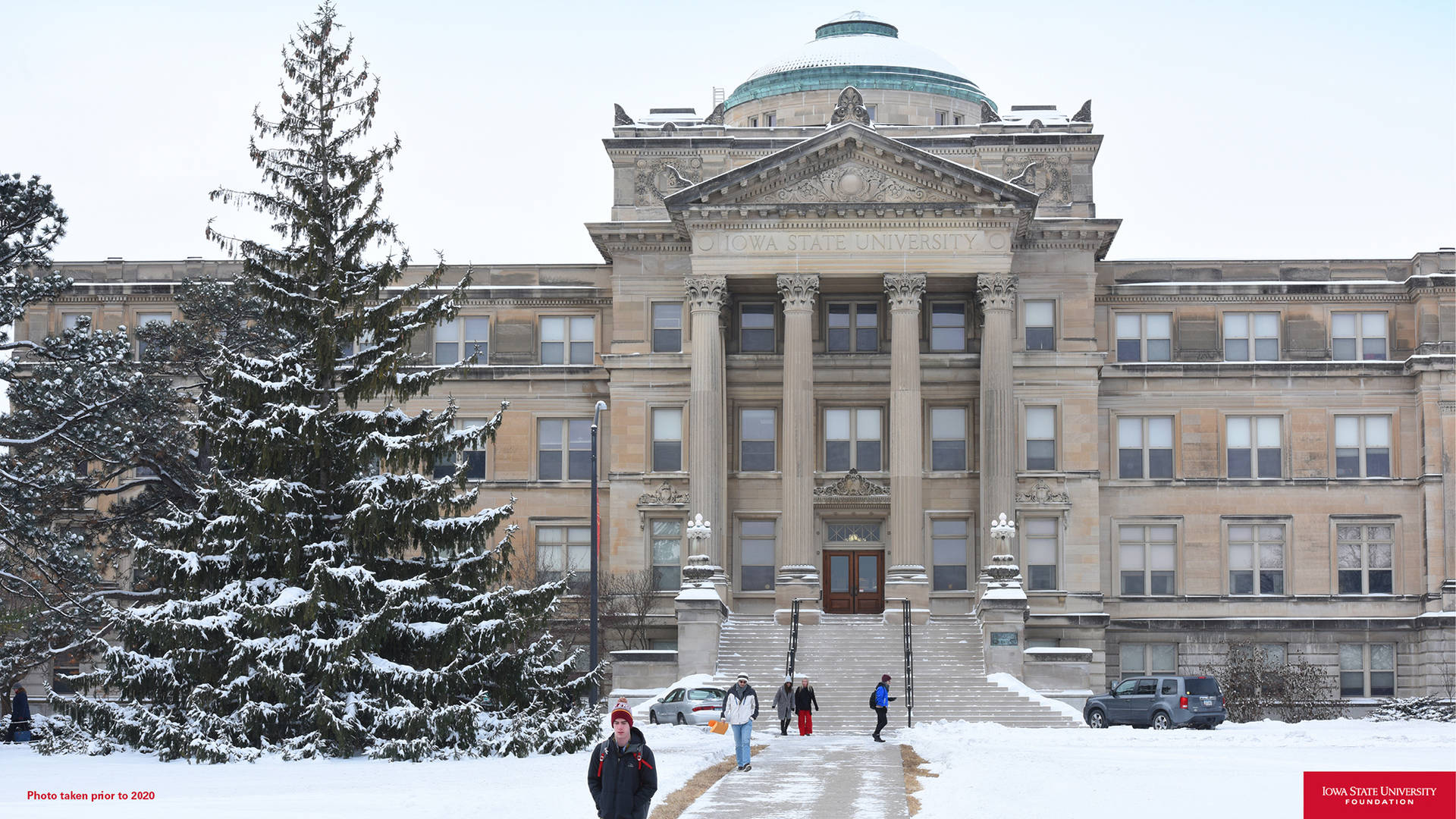 學生們在雪覆蓋樹木的大型大學建築附近的雪徑上行走。