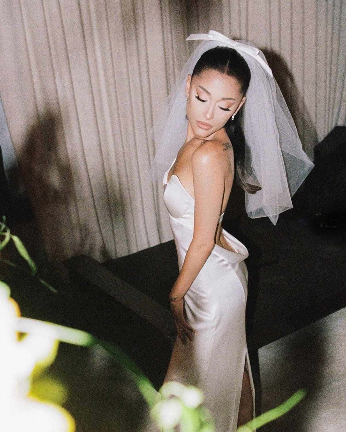 一位身穿白色緞面禮服和頭紗的新娘，在柔和的燈光和模糊的綠色植物中室內擺姿勢。