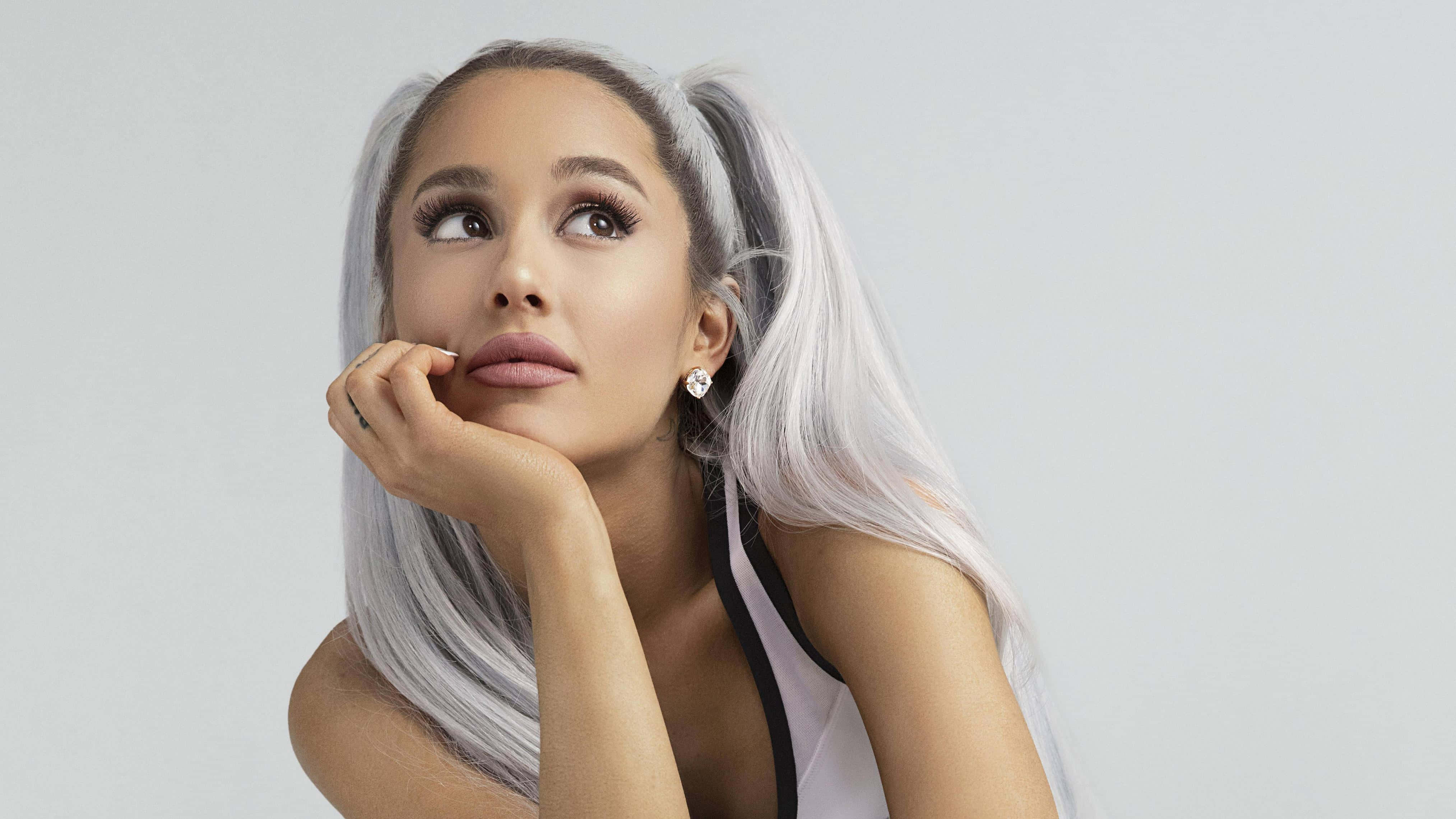 愛莉安娜·格蘭德展現她迷人的笑容 壁紙 — Ariana Grande 銀色孖辮造型，在純淺灰色背景前若有所思地向上望。