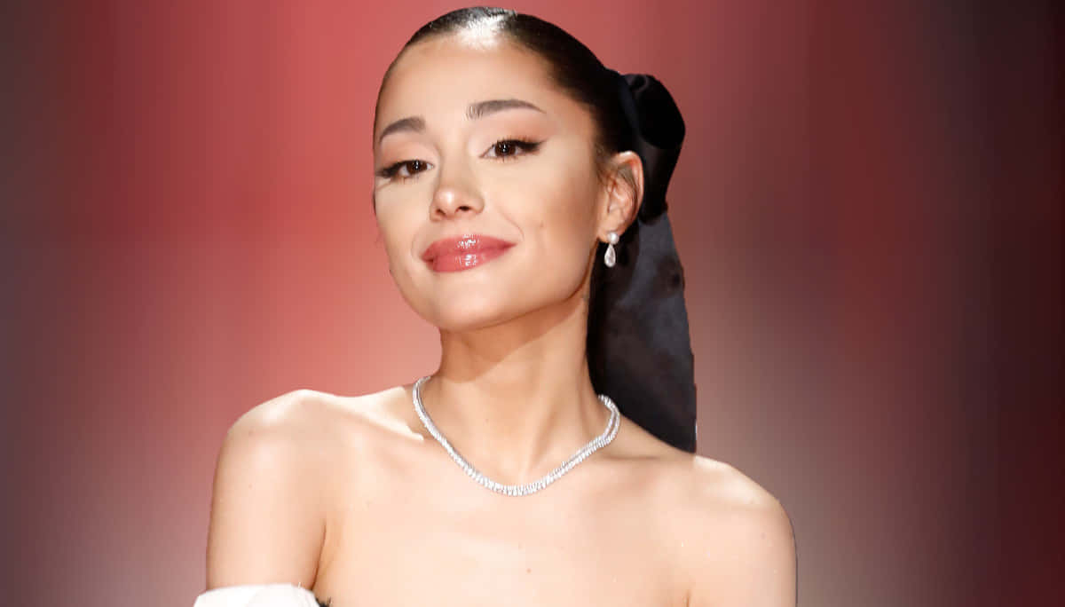 Ariana Grande 佩戴鑽石項鍊和耳環，頭髮紮成黑色蝴蝶結，以紅色背景為襯。