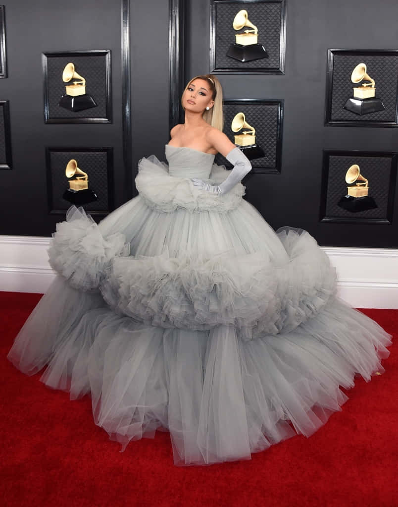 Ariana Grande 身穿灰色薄紗長裙企喺紅地毯上，身後有格林美獎座。