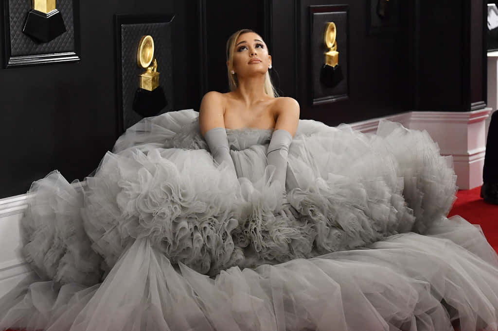 Ariana Grande 身穿灰色薄紗禮服，在紅地毯上擺姿勢，背景有格林美獎項。