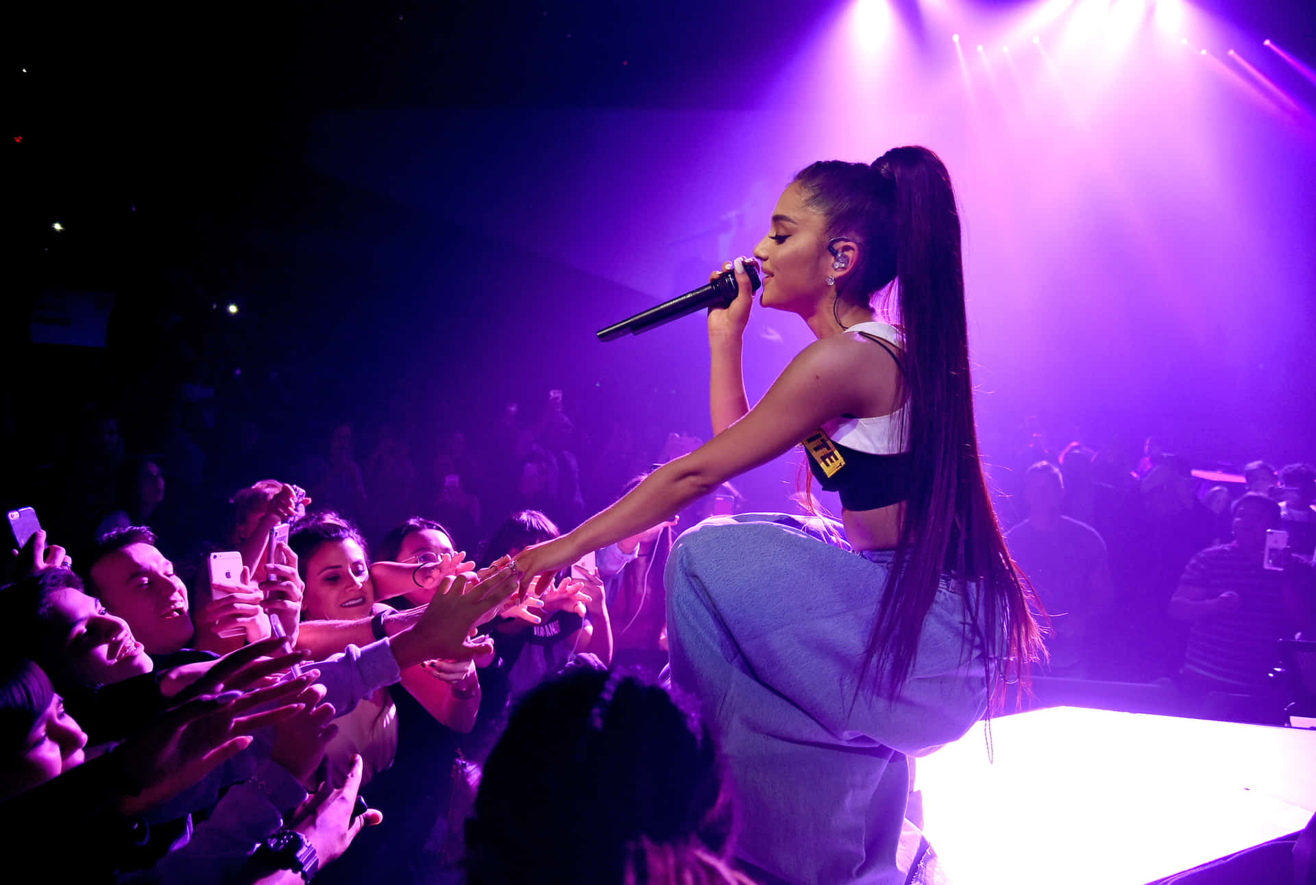 歌手 Ariana Grande 在舞台上表演，粉絲伸手觸摸她。