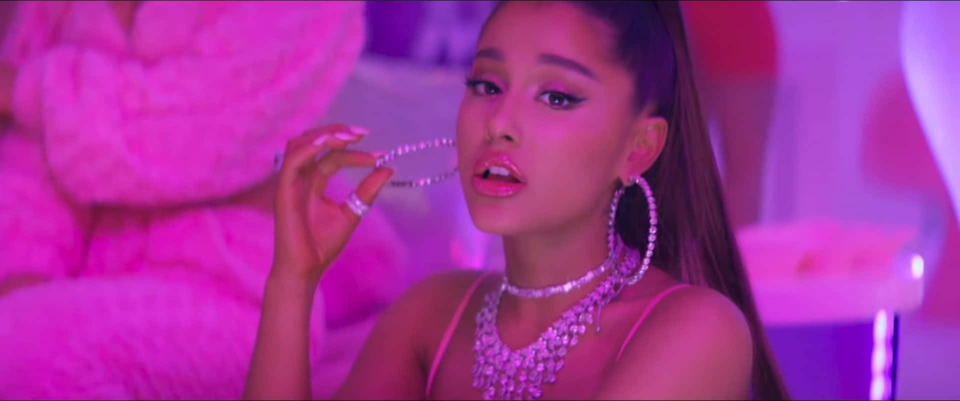 Ariana Grande 在霓虹粉紅房間中佩戴粉紅色珠寶和服裝。