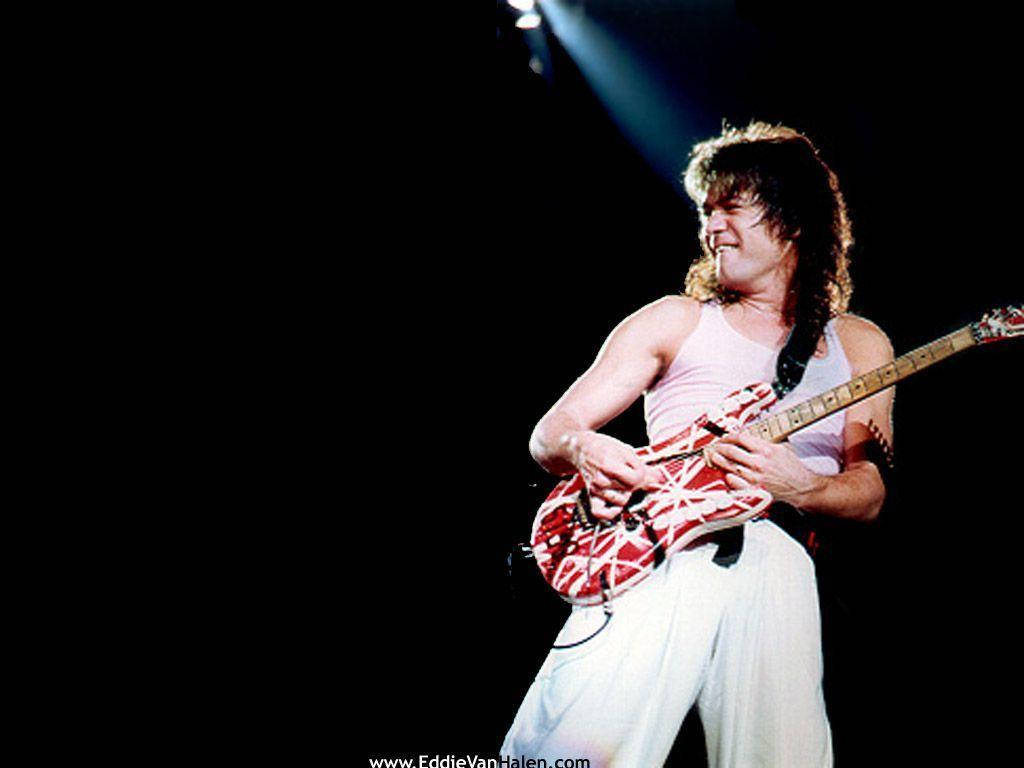 愛迪·范·海倫背心造型 壁紙 — Eddie Van Halen 在黑暗舞台的聚光燈下彈奏紅白條紋結他。