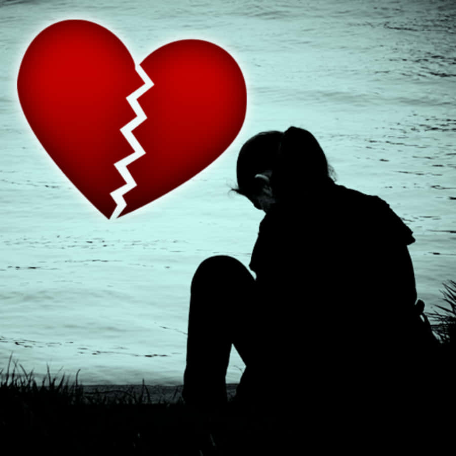 愛雖複雜，終究應帶來歡樂 壁紙 — 一個剪影人物坐在水邊，一個發光的紅色破碎心臟懸浮在他們上方。