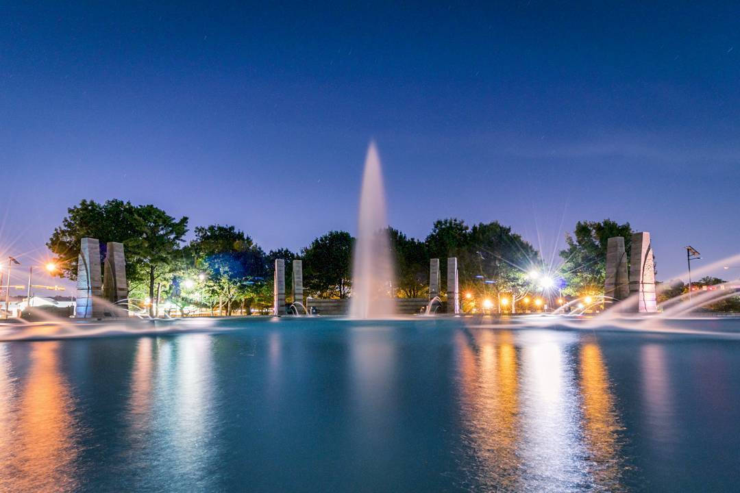夜間噴泉，燈光映照在水面，四周環繞樹木