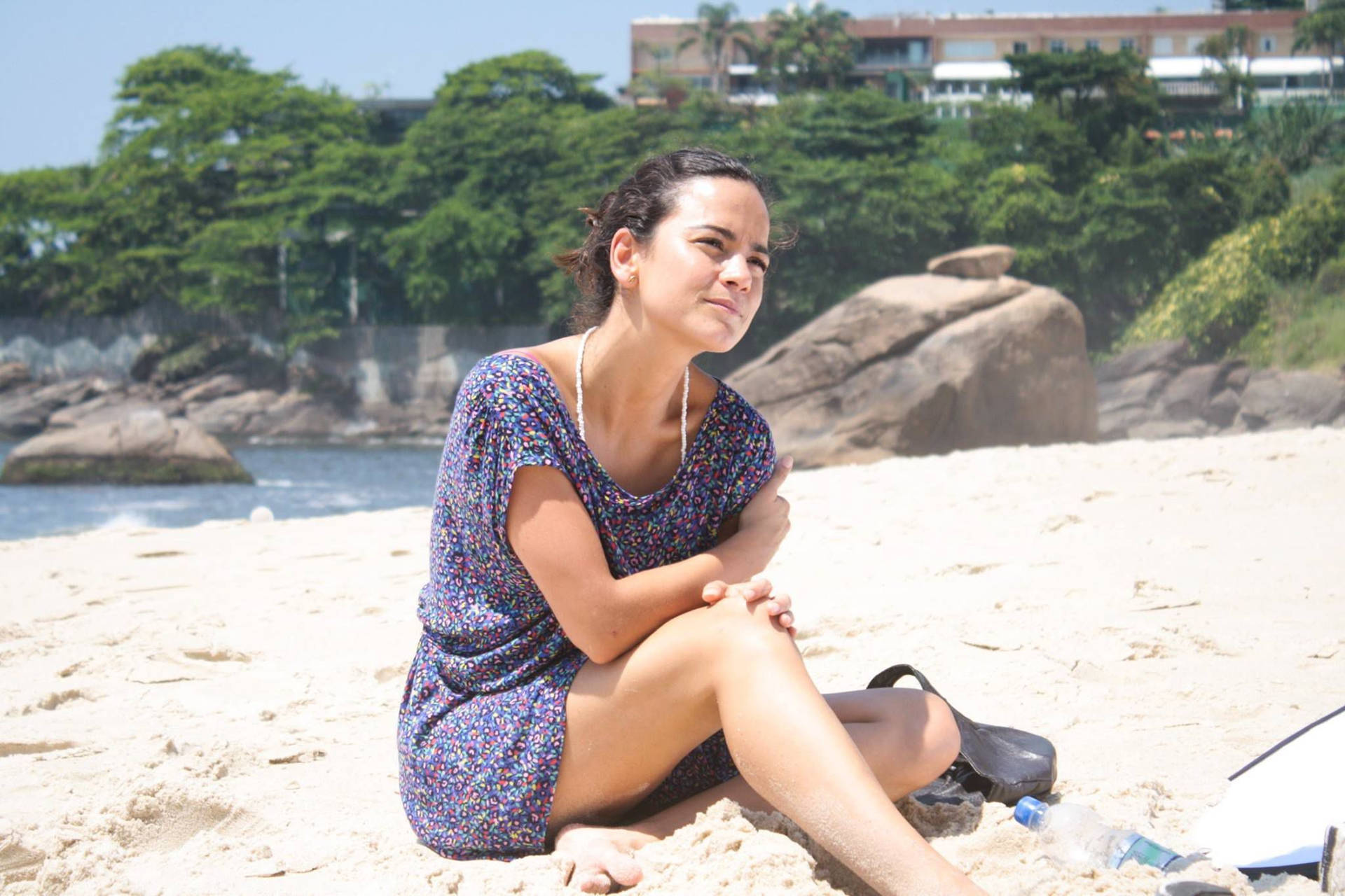 女性坐在沙灘上，背景有樹木和岩石