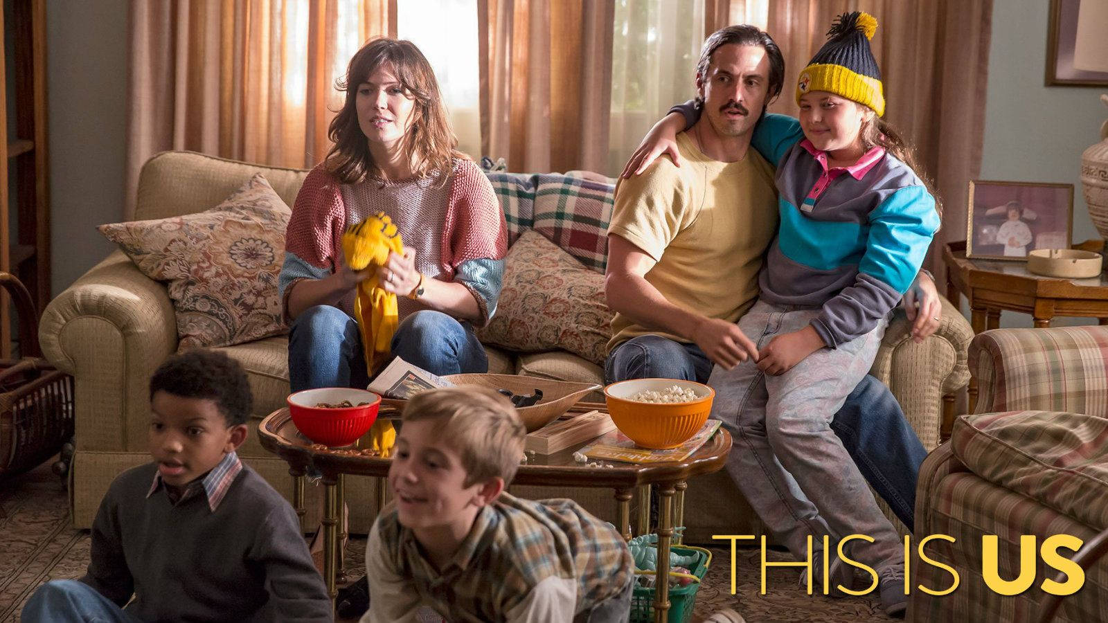 感人劇集《This Is US》中的Pearson家族 壁紙 — 一個五口之家一起坐在溫暖照明的客廳的沙發和地板上，一邊看電視一邊吃爆谷。