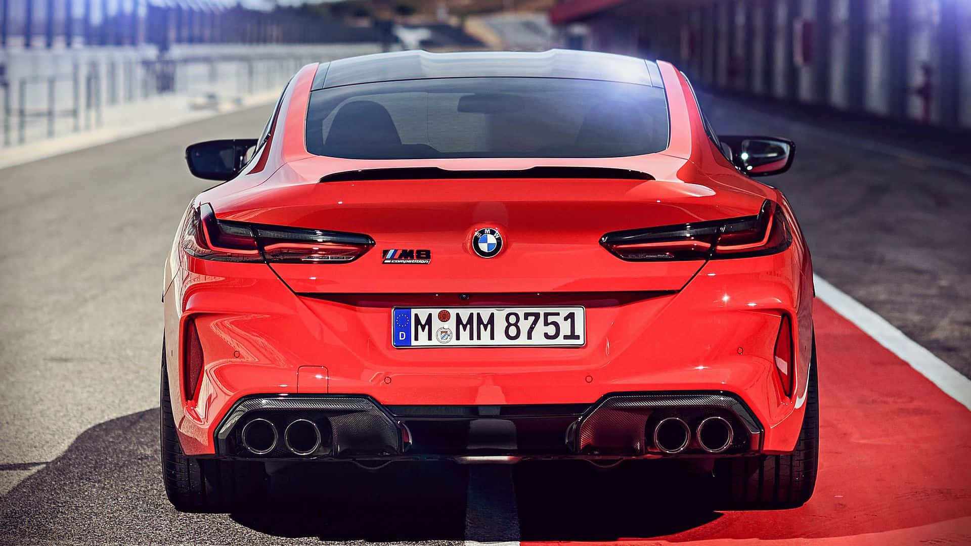 賽道上紅色BMW M8 Coupe的後視圖，配備四出排氣管和發光尾燈。