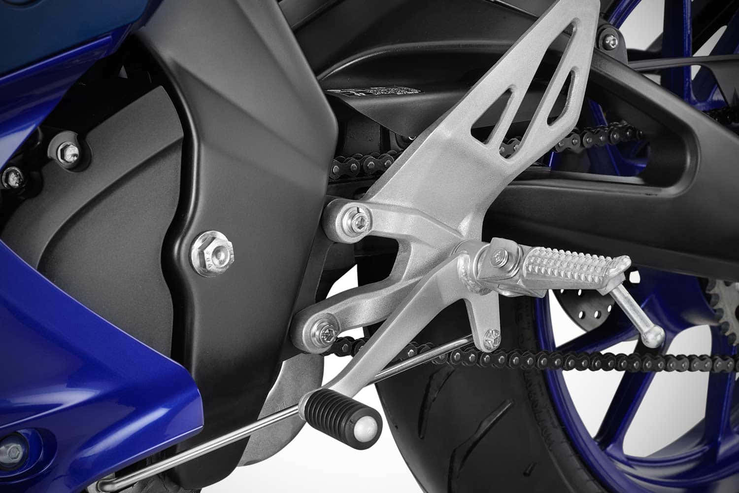 感受 MotoGP 競速的激情 — R15 壁紙 — 白色背景上，藍色電單車的銀色腳踏、鏈條和後輪特寫。